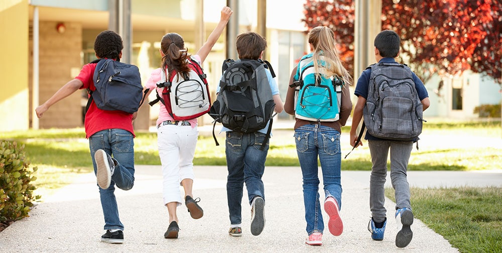 Fünf Schulkinder mit Tagessrucksäcken vor einer Schule